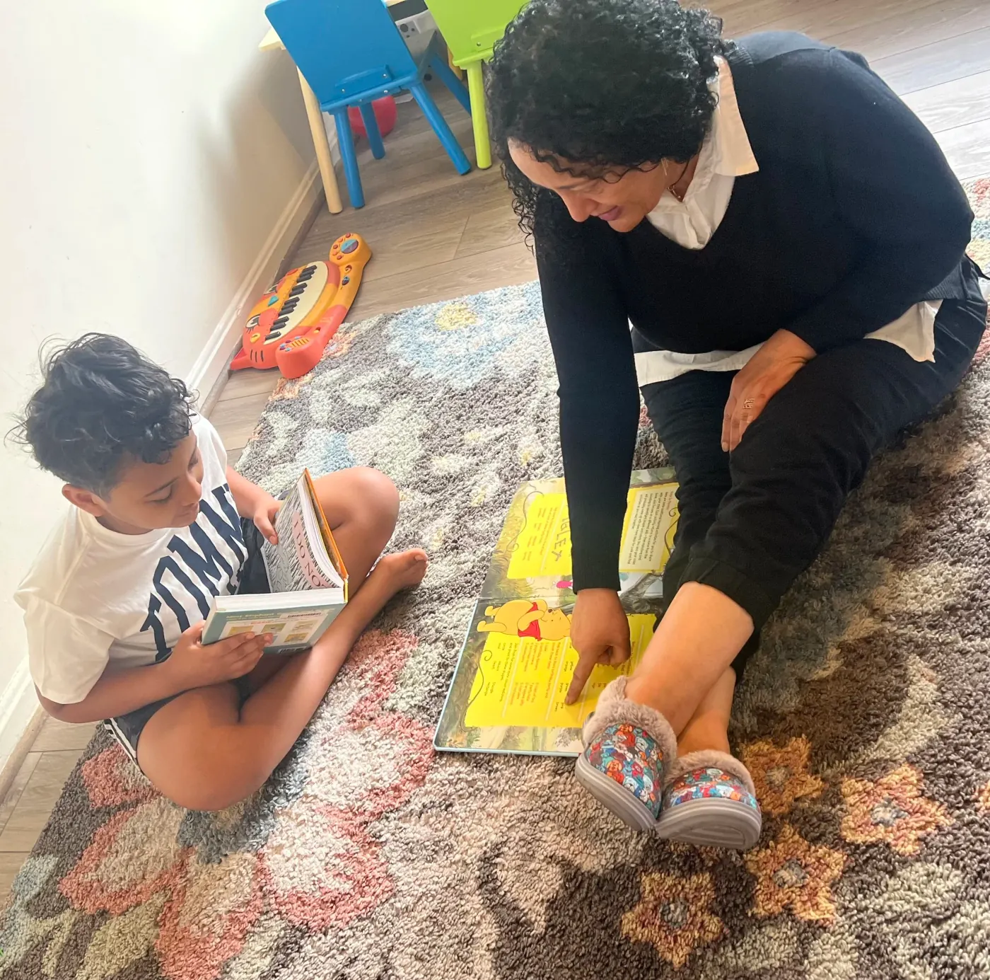 Yewerk Getu sitting on a play rug with a young child, pointing at the page of a picture book as he reads alongside her.